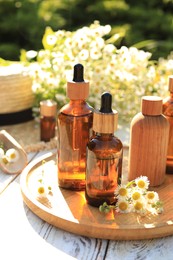 Photo of Bottles of essential oil and flowers on white wooden table outdoors