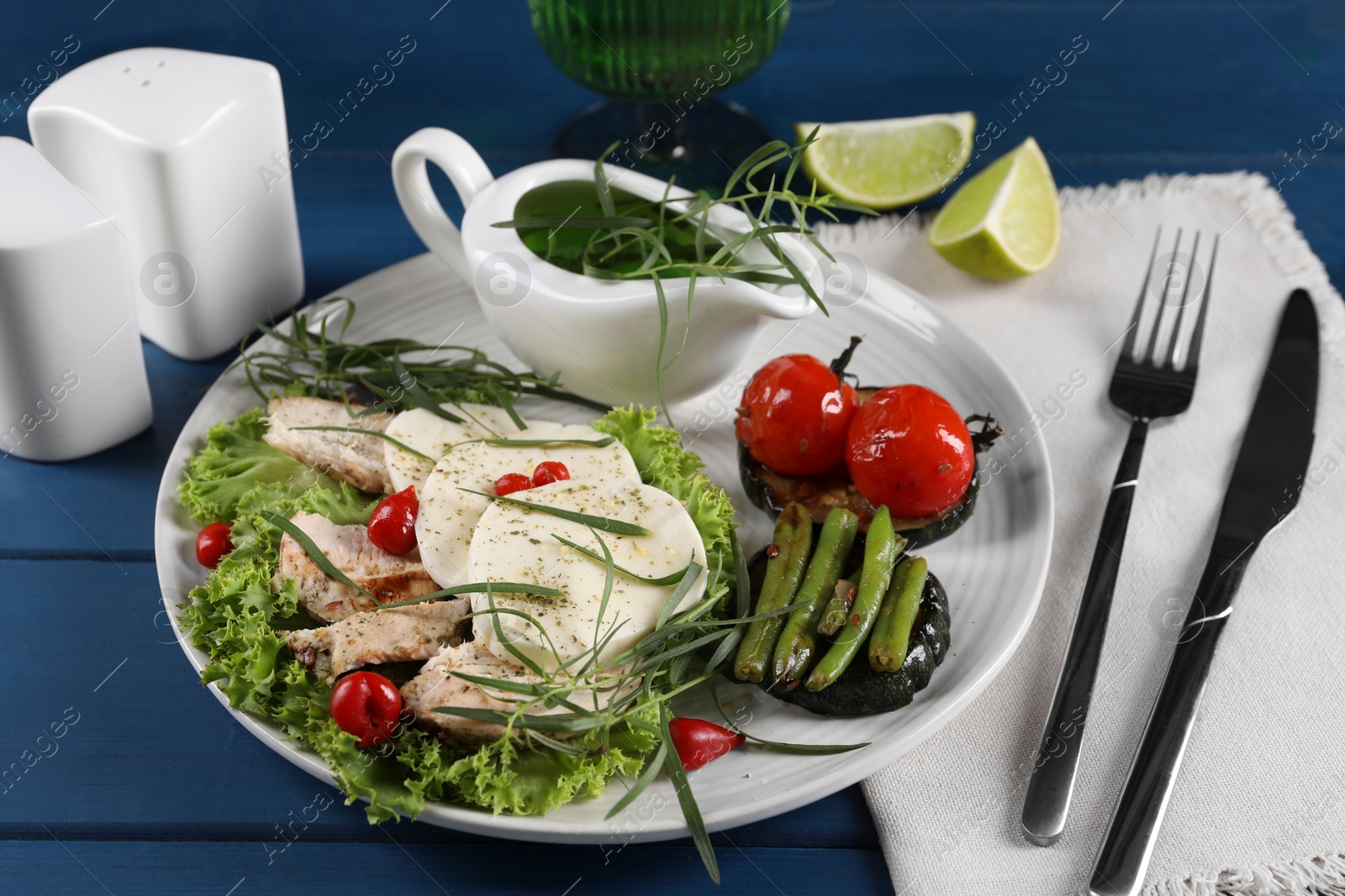 Photo of Tasty mozzarella, chicken and vegetables with tarragon served on blue wooden table, closeup