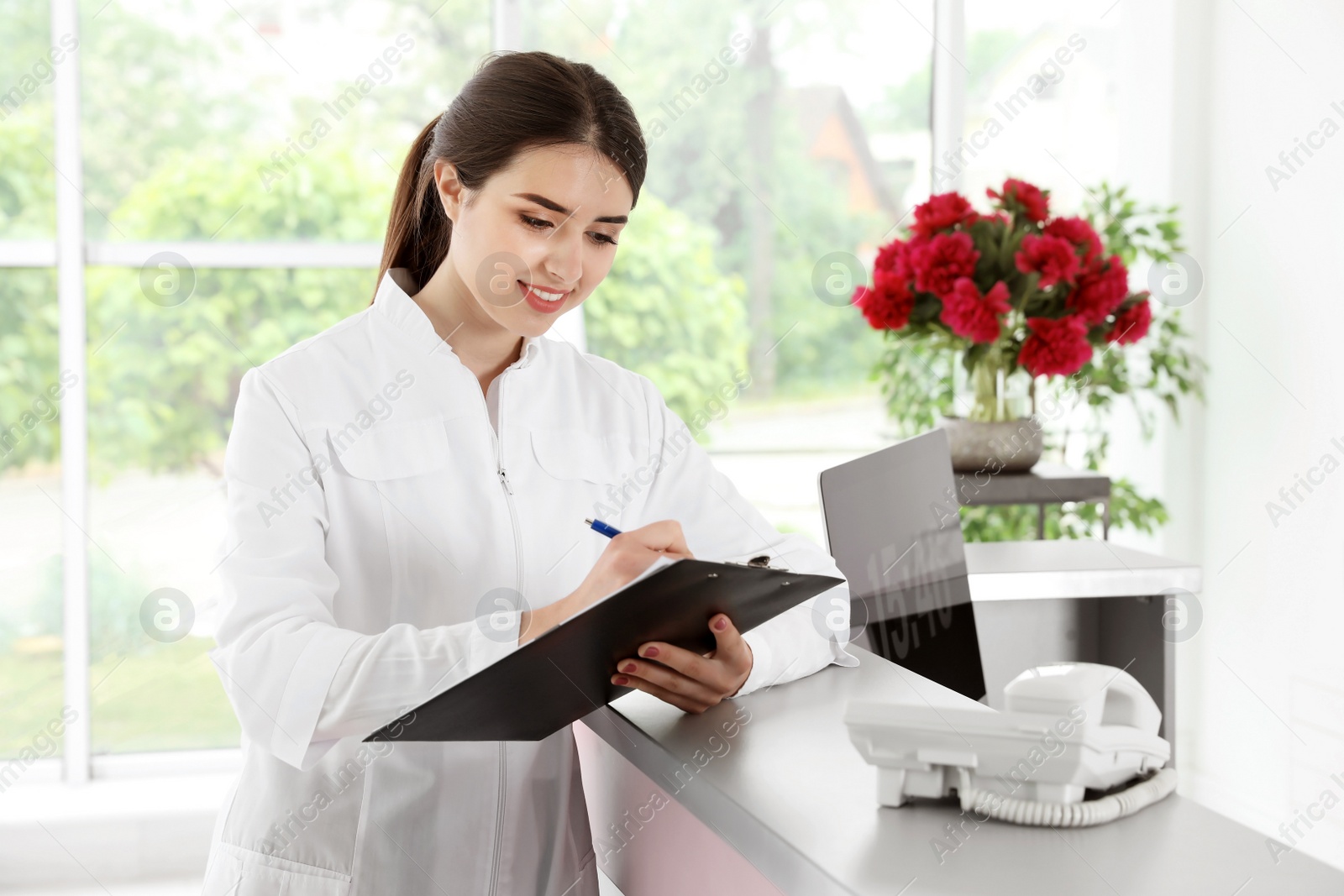 Photo of Young receptionist with clipboard at desk in beauty salon