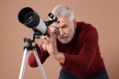Senior astronomer looking at stars through telescope on brown background