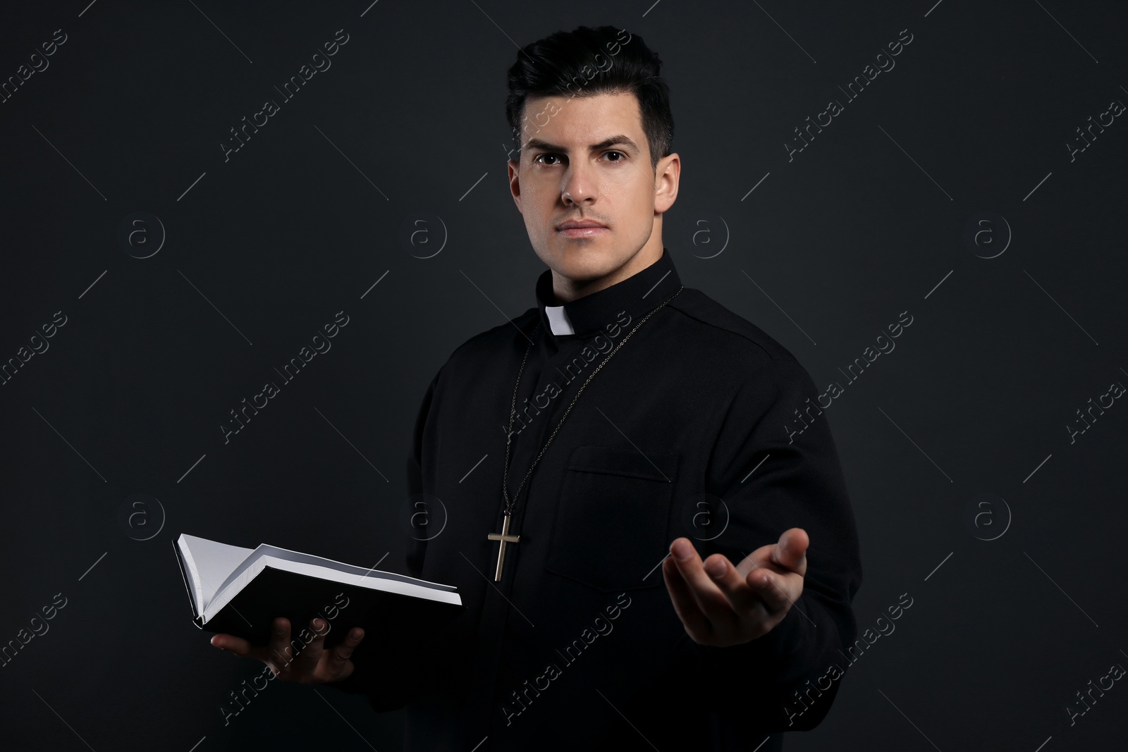 Photo of Priest in cassock with Bible on black background