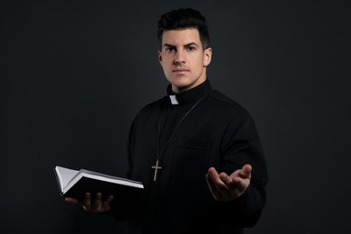 Priest in cassock with Bible on black background