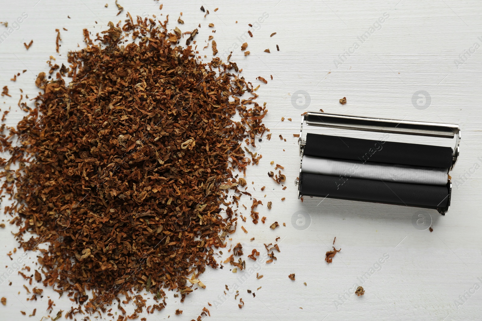 Photo of Roller with hand rolled cigarette and tobacco on white wooden table, flat lay