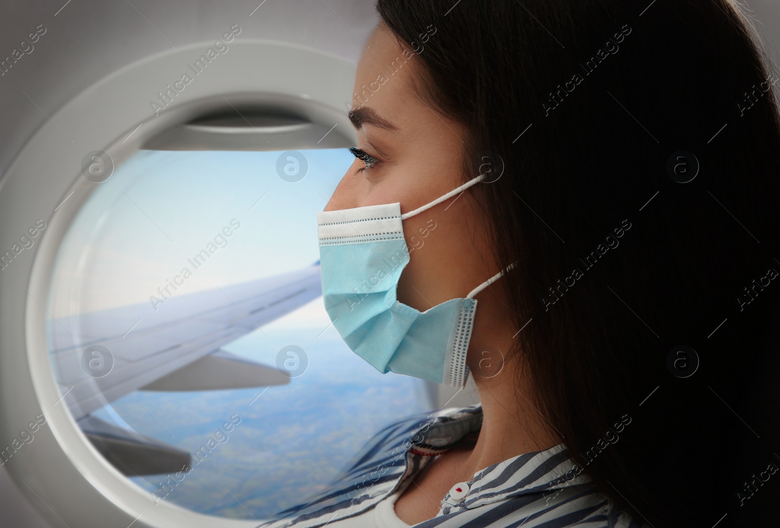 Image of Traveling by airplane during coronavirus pandemic. Woman with face mask near porthole