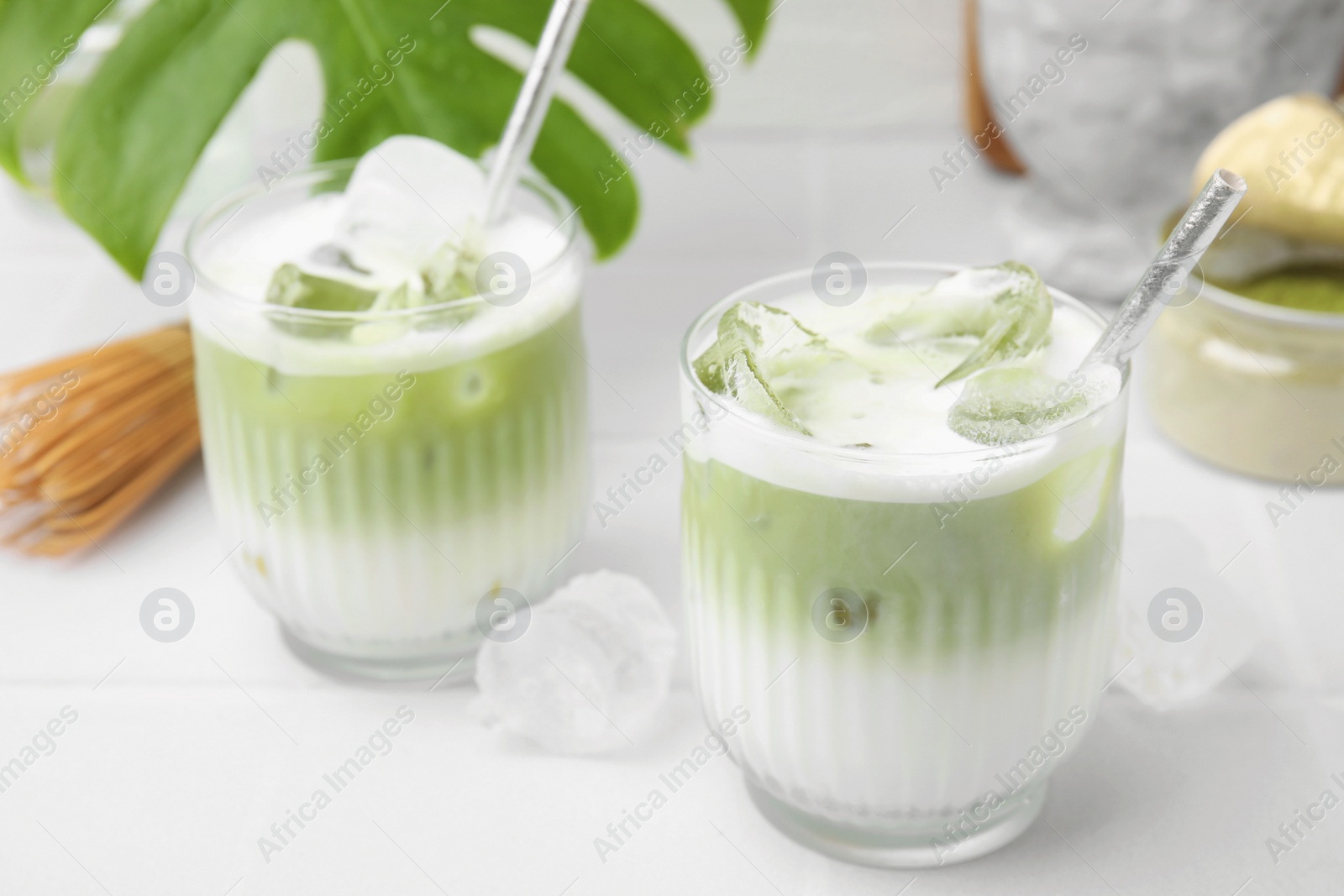 Photo of Glasses of tasty iced matcha latte on white tiled table