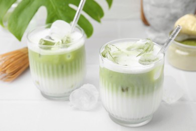 Photo of Glasses of tasty iced matcha latte on white tiled table