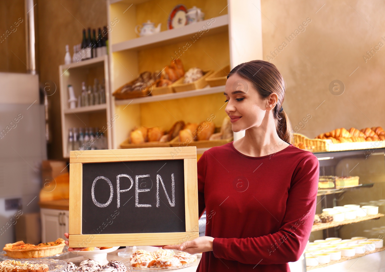 Photo of Female business owner holding OPEN sign in bakery