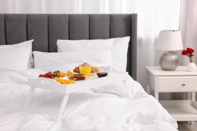 Photo of Tray with delicious breakfast on bed in room