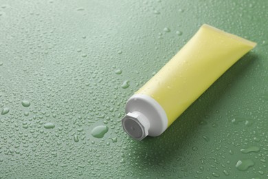 Photo of Moisturizing cream in tube on green background with water drops, closeup. Space for text