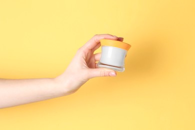 Photo of Woman holding jar of cream on yellow background, closeup