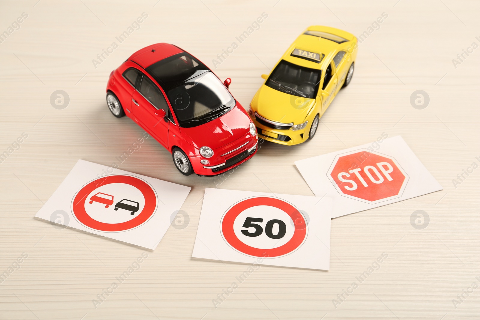 Photo of Cards with different road signs and toy cars on white wooden table. Driving school