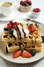 Photo of Delicious Belgian waffles with ice cream, berries and chocolate sauce served on white table, closeup