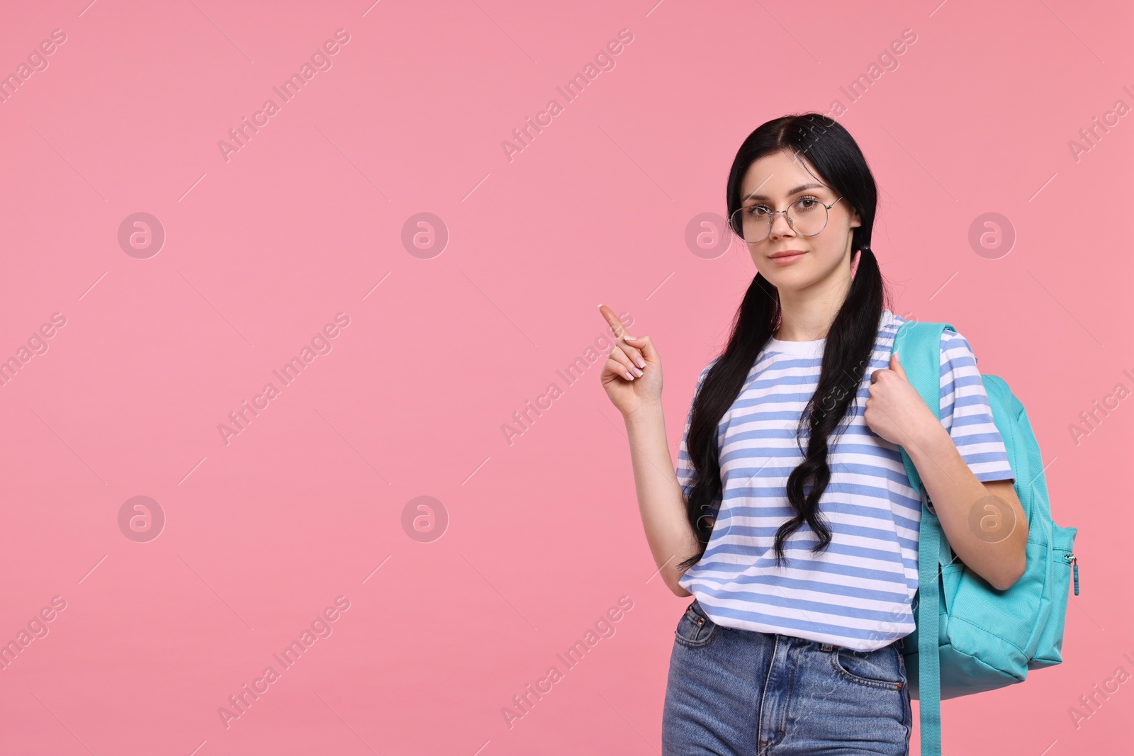 Photo of Student with backpack pointing at something on pink background. Space for text