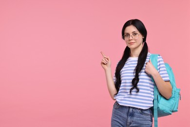 Photo of Student with backpack pointing at something on pink background. Space for text