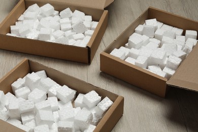 Photo of Open cardboard boxes with pieces of polystyrene foam on wooden floor. Packaging goods