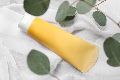 Tube of face cleansing product and eucalyptus leaves on white fabric