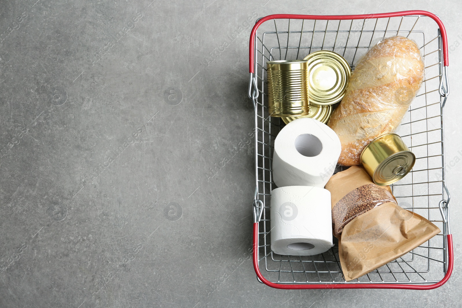 Photo of Top view of shopping basket with products and toilet paper rolls on light grey stone table, space for text. Panic caused by virus