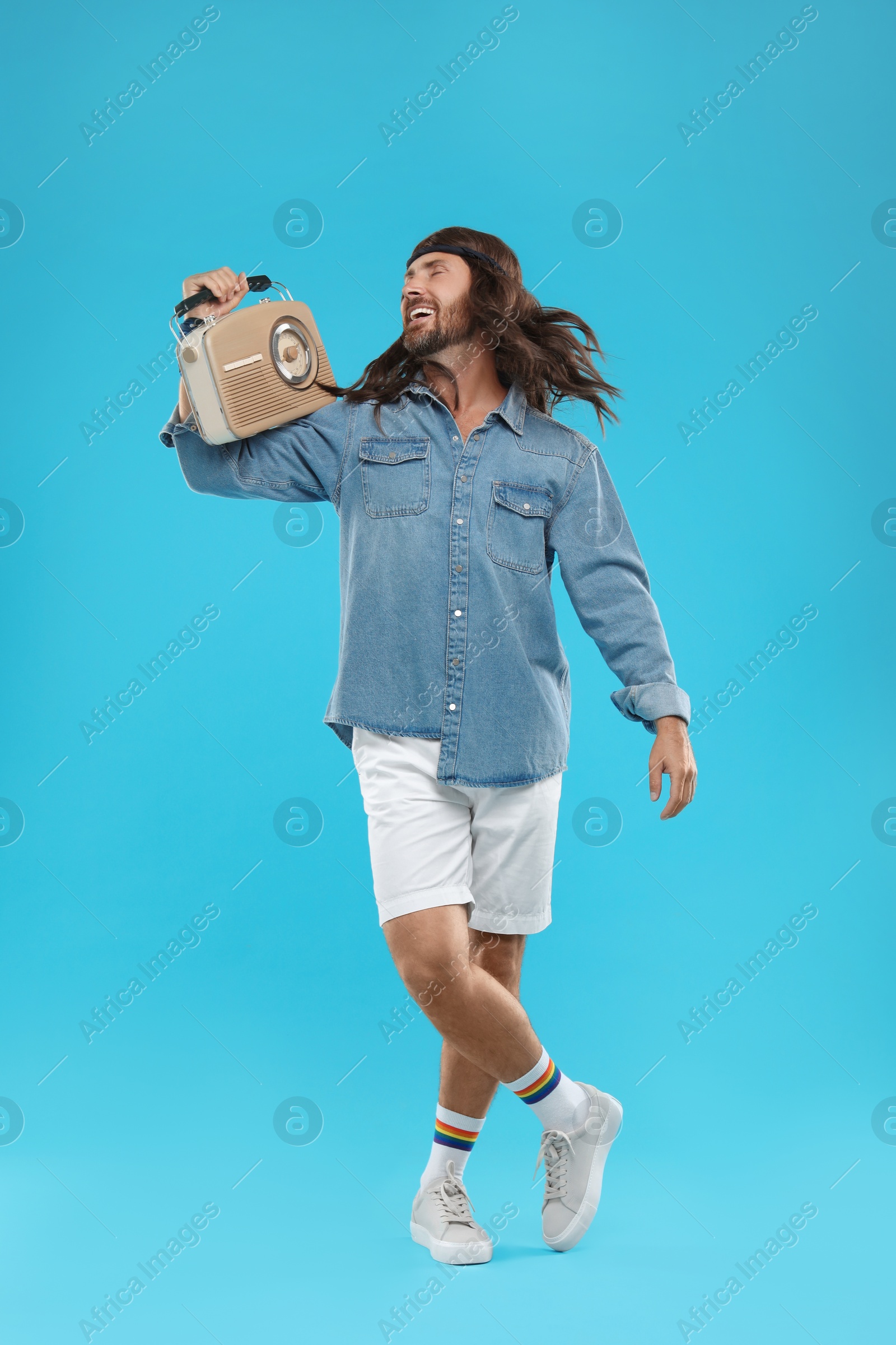 Photo of Stylish hippie man with retro radio receiver on light blue background