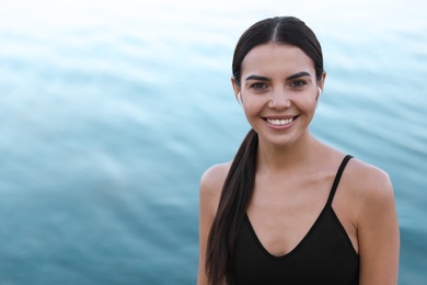 Photo of Young sportswoman with wireless earphones near river