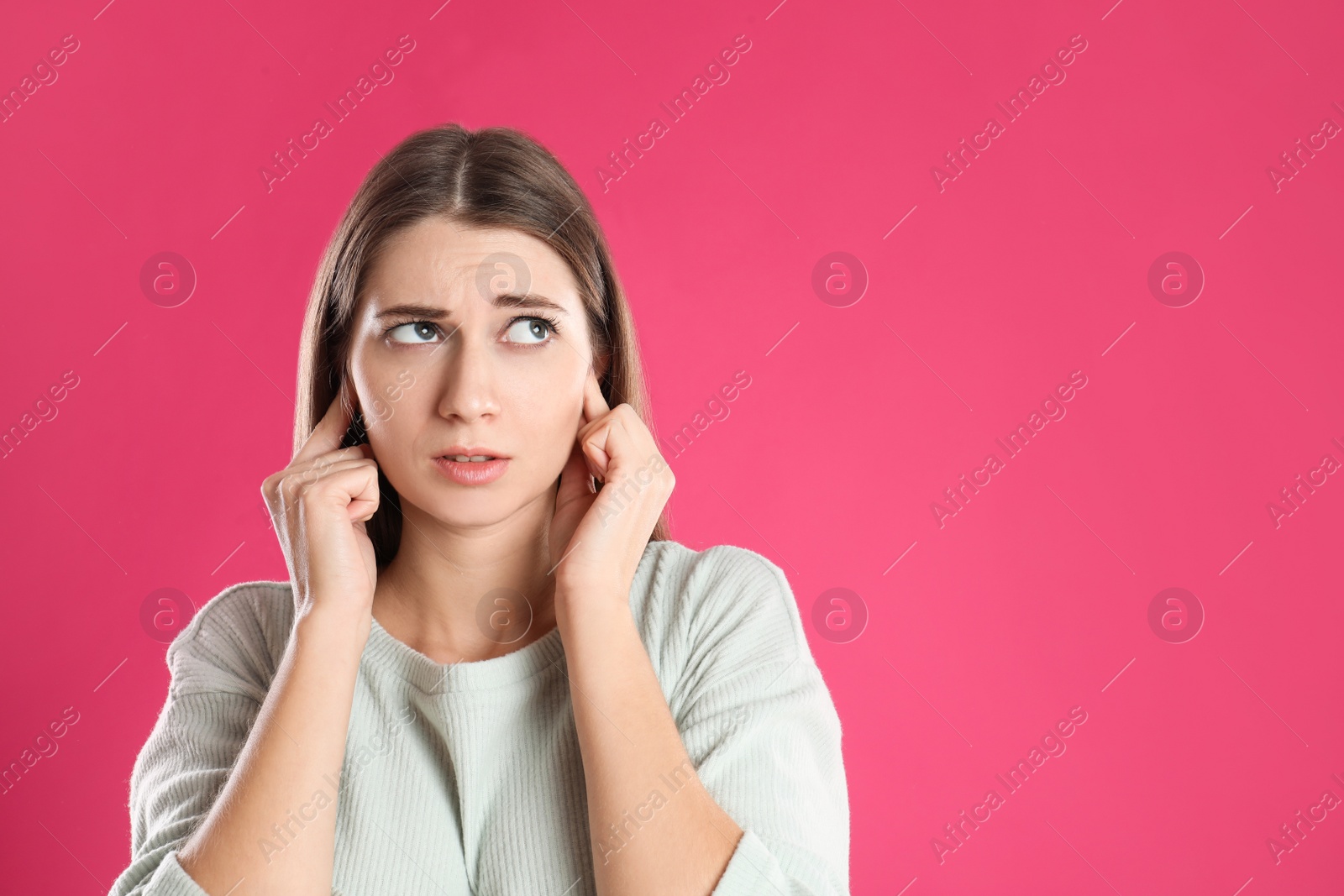 Photo of Emotional young woman covering her ears with fingers on pink background. Space for text