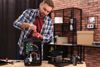 Man with screwdriver fixing coffee machine at table indoors