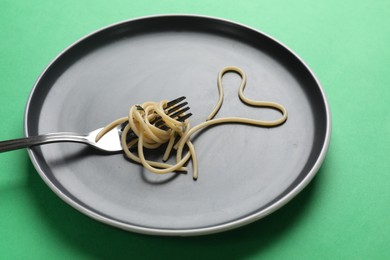 Photo of Heart made of tasty spaghetti and fork on green background
