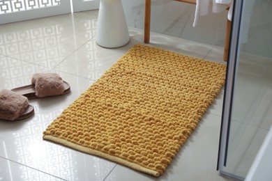 Photo of Soft orange bath mat and slippers on floor indoors