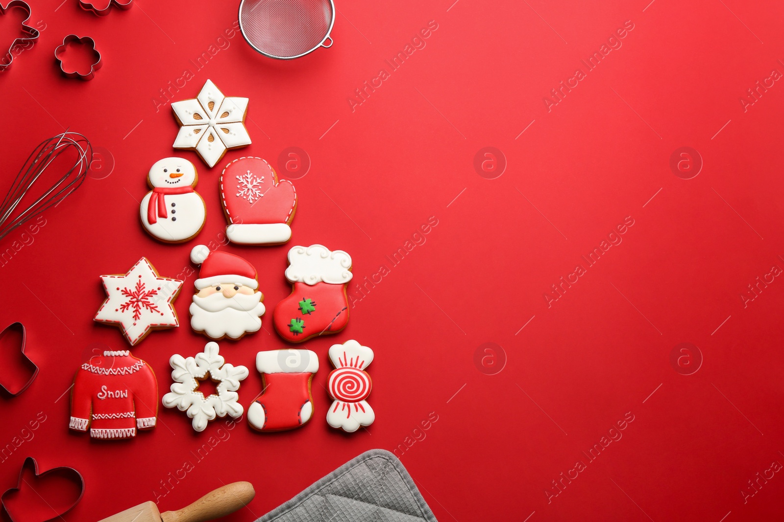 Photo of Kitchen utensils near Christmas tree shape made of delicious gingerbread cookies on red background, flat lay. Space for text