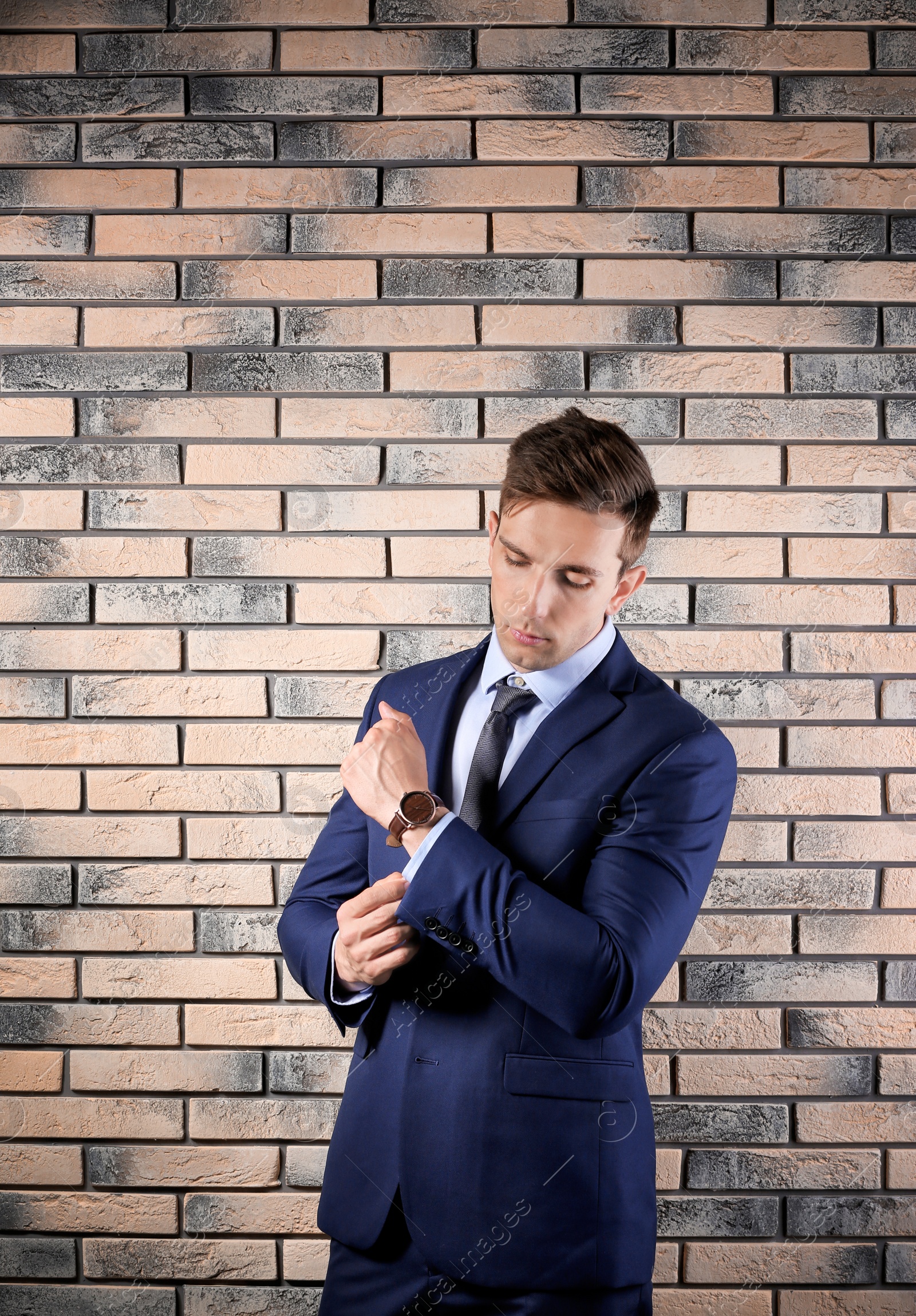 Photo of Handsome young man in suit near brick wall background