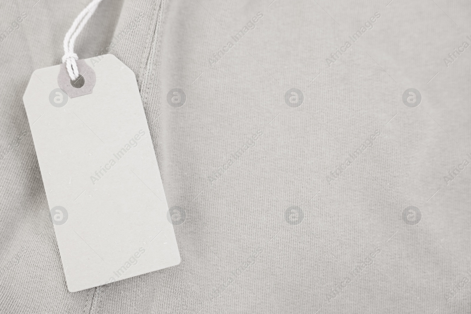 Photo of Cardboard tag on beige garment, top view. Space for text