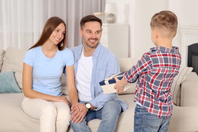 Photo of Little boy presenting his parents with gift at home