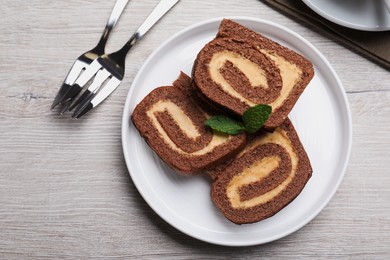 Tasty chocolate cake roll with cream and mint on light wooden table, flat lay