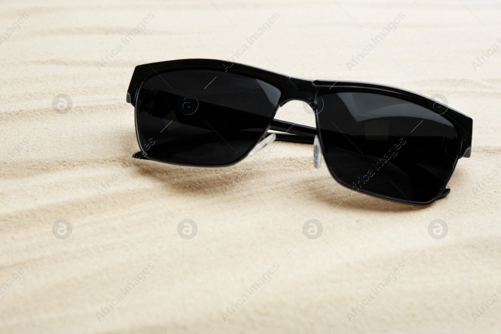 Photo of Stylish sunglasses on white sand. Summer time