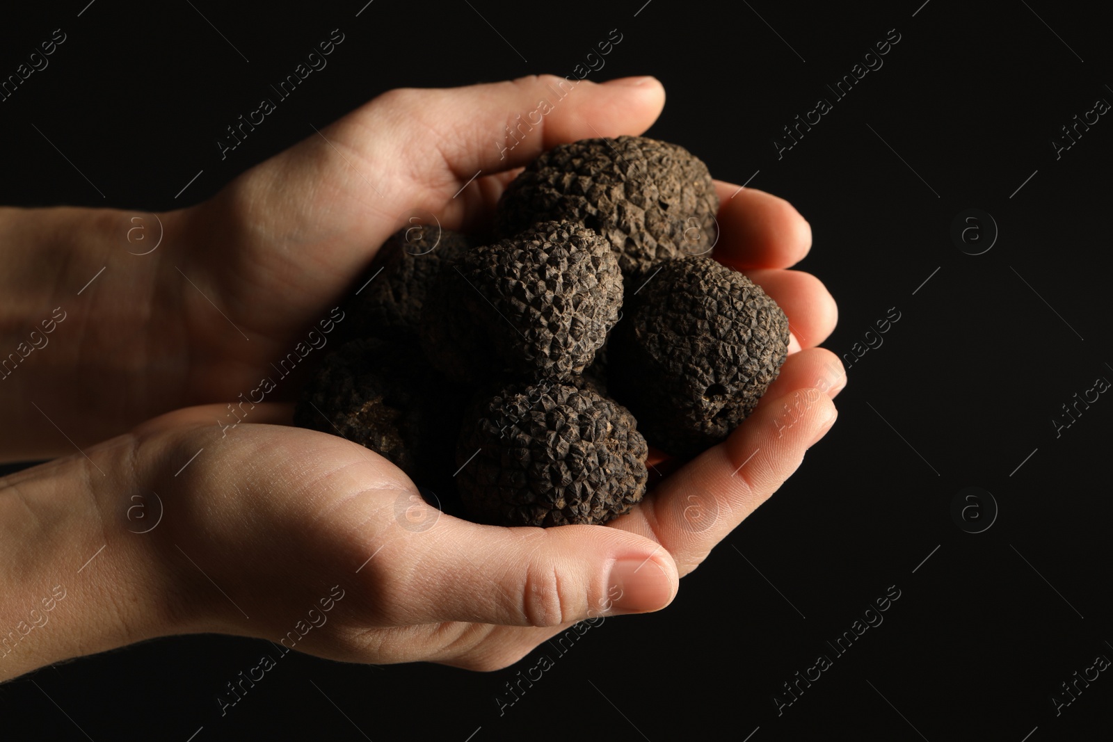 Photo of Woman holding heap of truffles in hands on black background, closeup