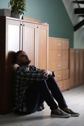 Photo of Depressed young man sitting on floor in kitchen