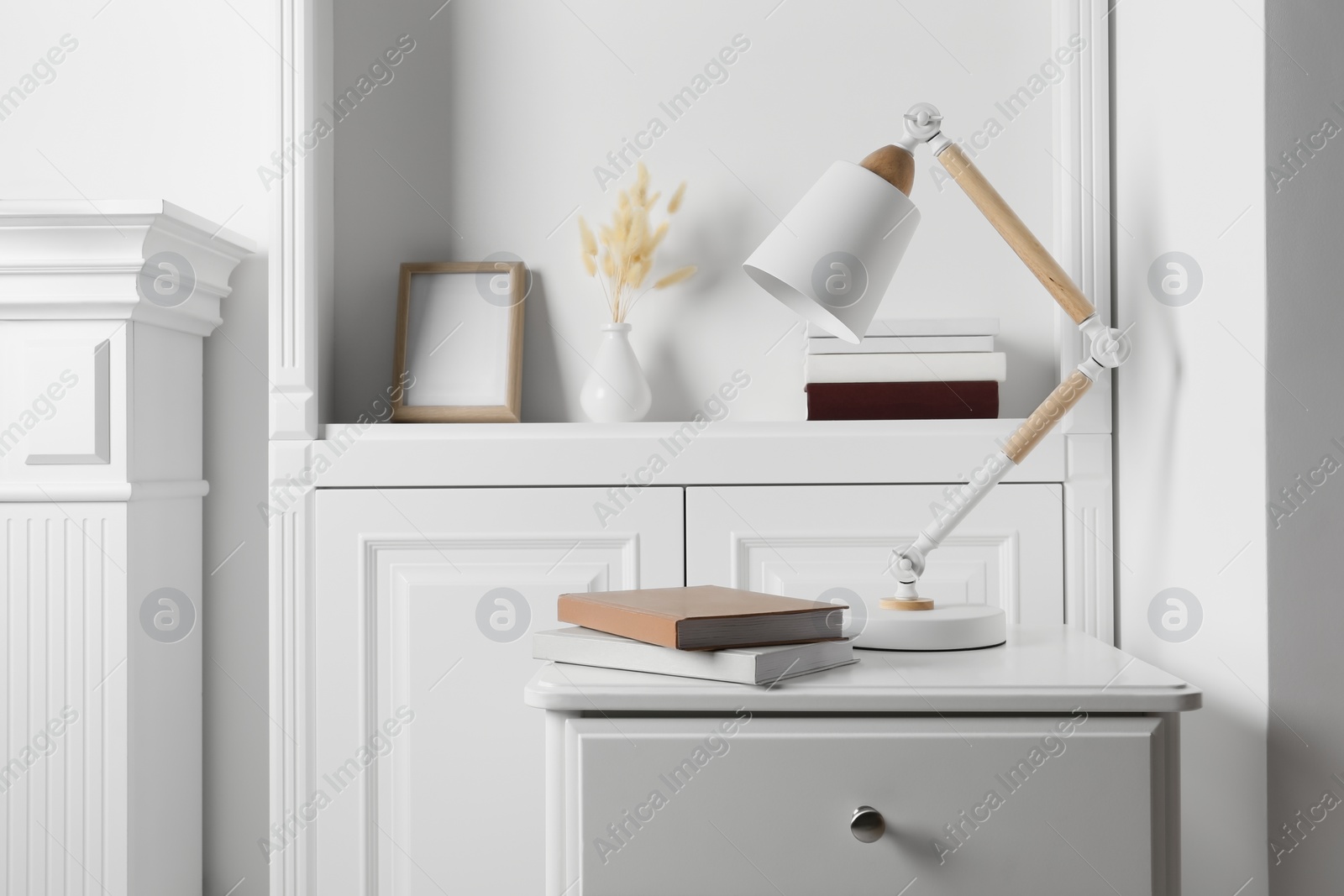 Photo of Stylish lamp and books on white side table in light room. Interior design