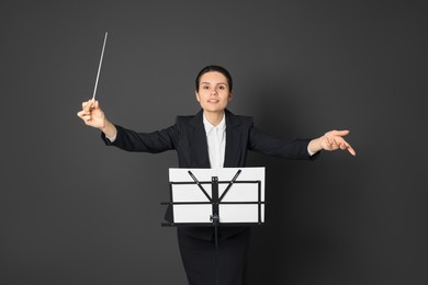 Happy professional conductor with baton and note stand on grey background