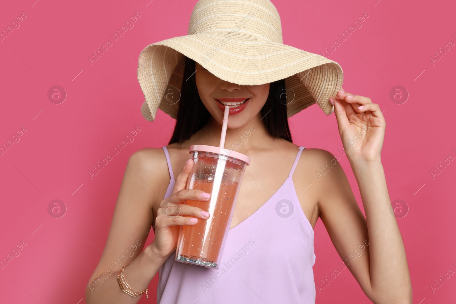 Photo of Beautiful young woman with straw hat and glass of refreshing drink on pink background