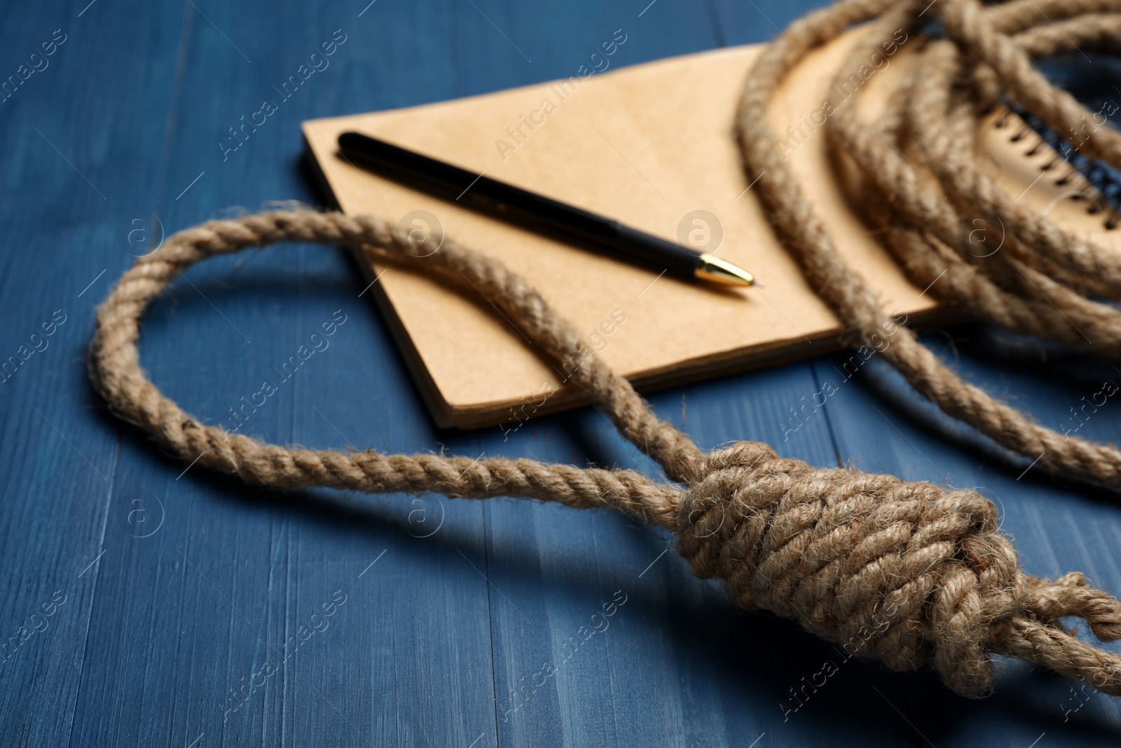 Photo of Rope noose and blank notebook with pen on blue wooden table, closeup