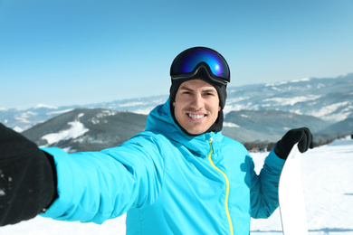 Photo of Happy man with snowboard taking selfie in mountains. Winter vacation