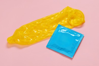 Photo of Unrolled condom and package on pink background. Safe sex