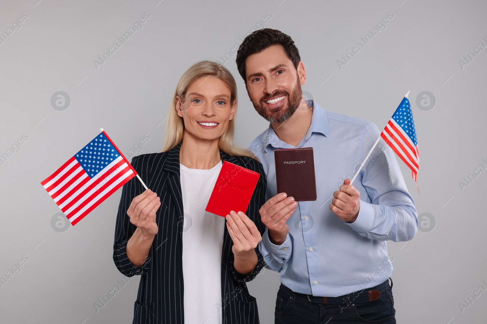 Photo of Immigration. Happy couple with passports and American flags on gray background