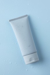 Moisturizing cream in tube on light blue background with water drops, top view