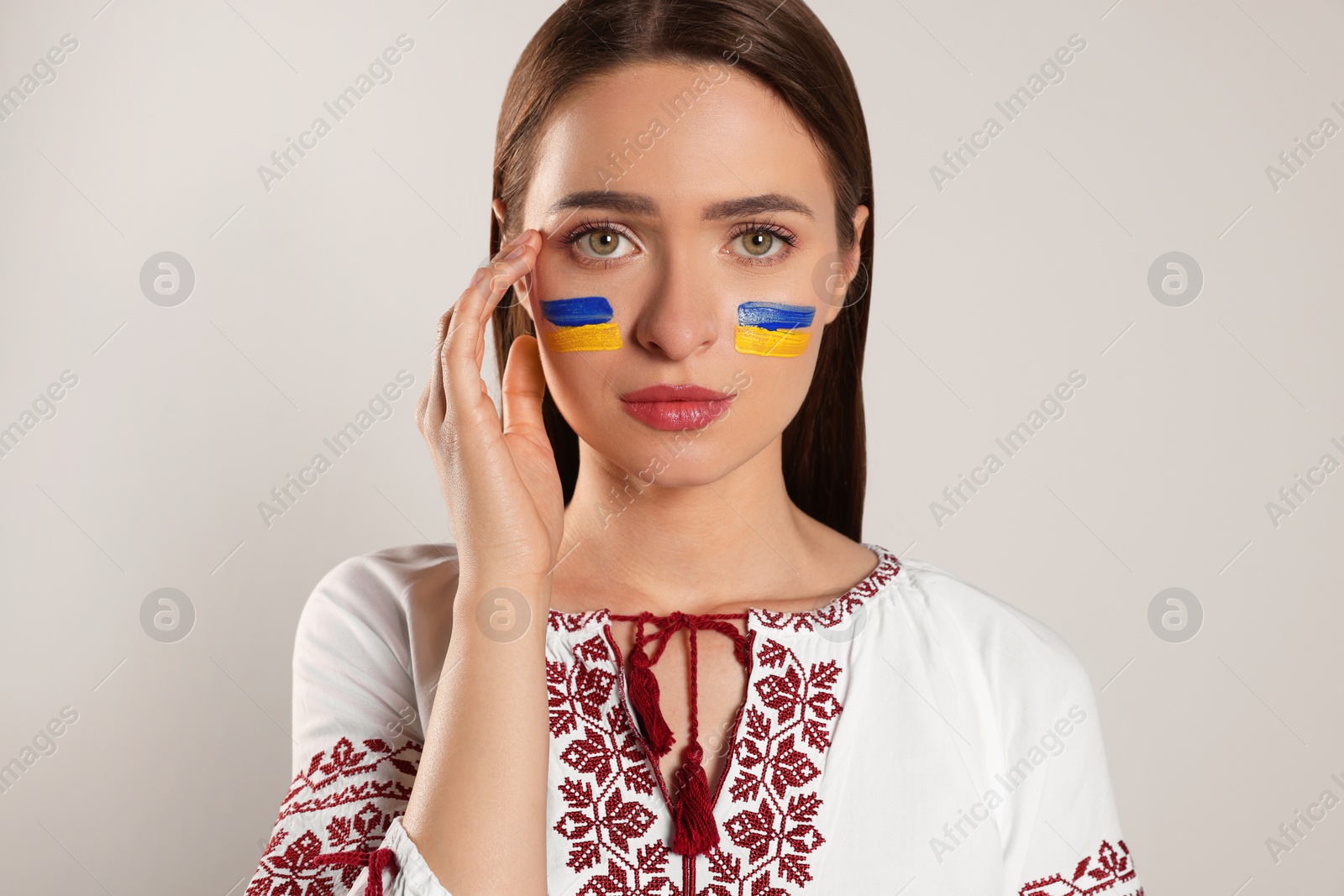 Photo of Young woman with drawings of Ukrainian flag on face against beige background