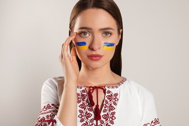 Photo of Young woman with drawings of Ukrainian flag on face against beige background