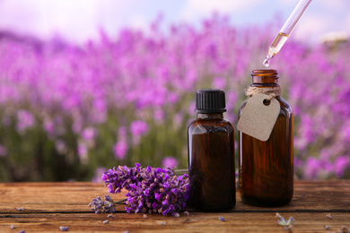 Photo of Dripping essential oil from pipette into bottle near lavender flowers on wooden table, closeup. Space for text