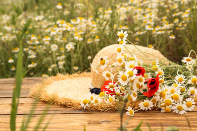 Photo of Bouquet of poppies and chamomiles with straw hat on wooden table outdoors