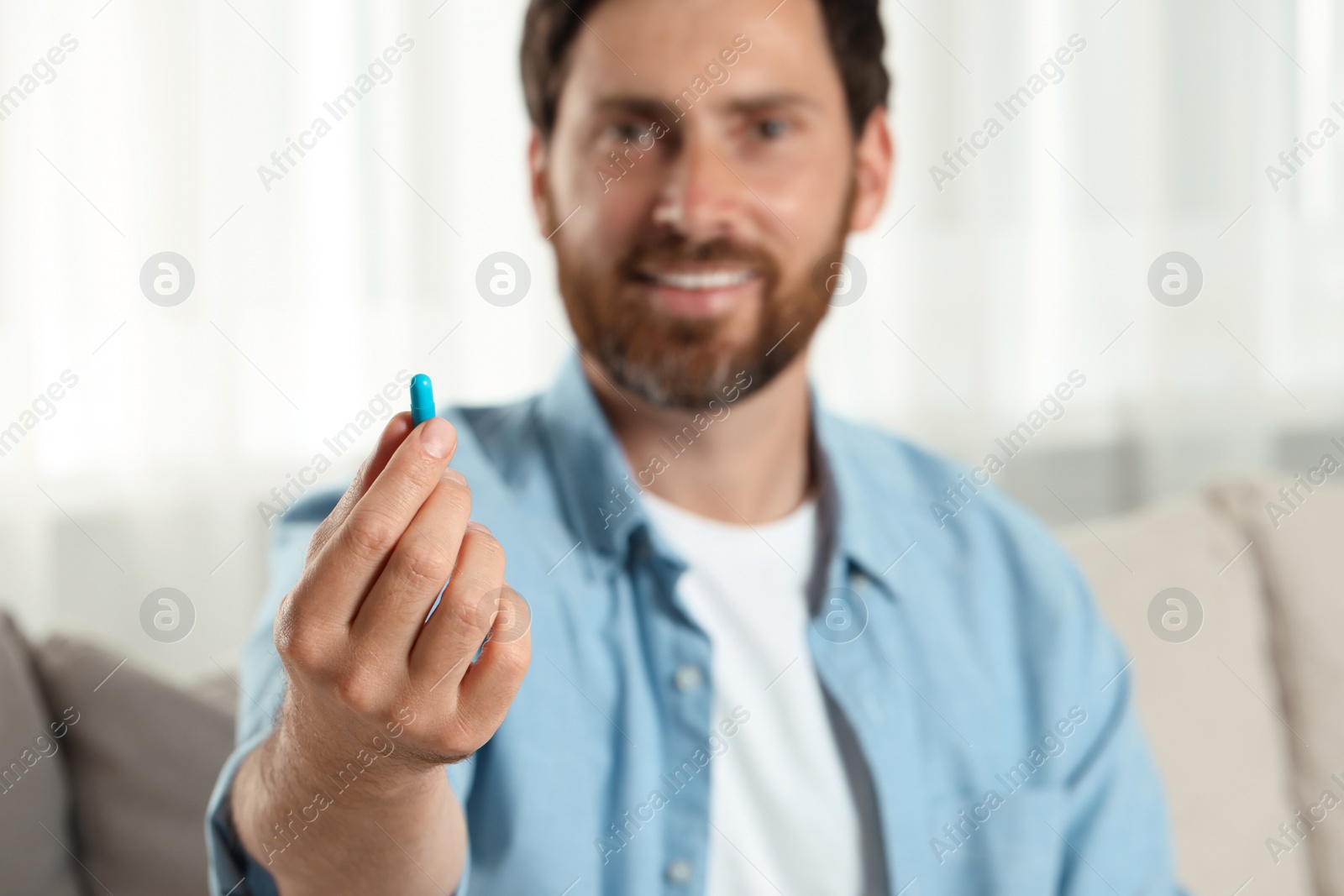 Photo of Handsome man with pill at home, selective focus