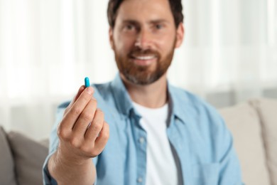 Handsome man with pill at home, selective focus