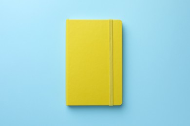 Photo of Closed yellow notebook on light blue background, top view